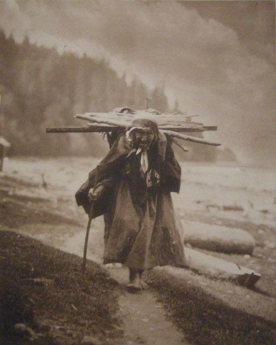 Native women carrying personal belongings, possibly wood for fire.