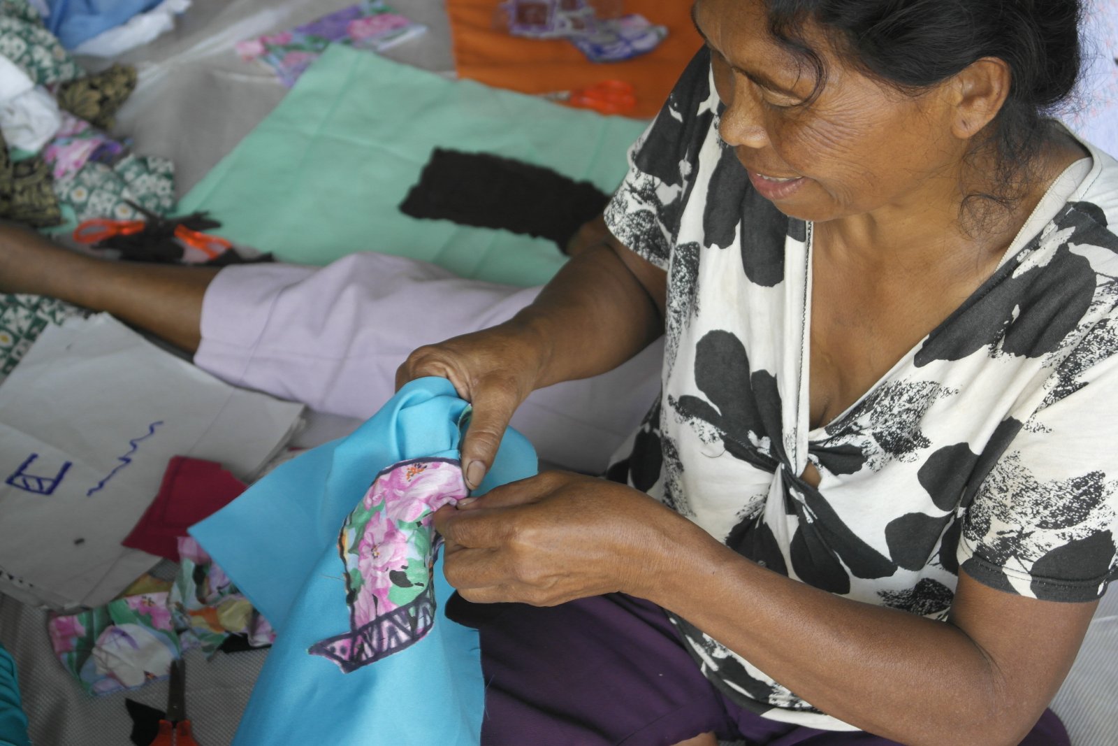 A participant threads running stitches over the dwelling she dreams of coming home to upon resettlement. Photo by libudsuroy